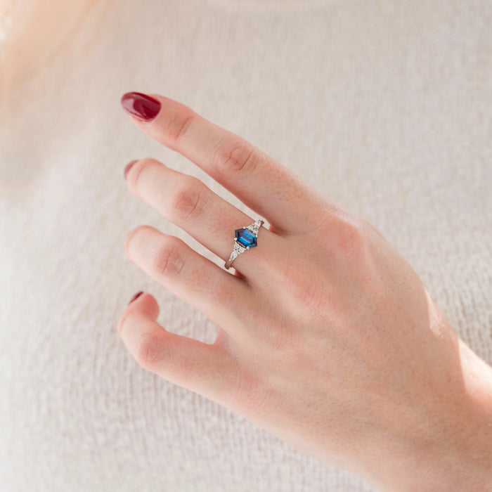 Sonnet Hexagon Cut Alexandrite Engagement Ring in 14K White Gold featuring a bold blue hexagon-cut alexandrite with tapered diamond accents, photographed on a hand by Aquamarise Gold.