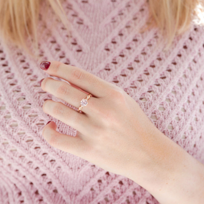 Hand wearing a diamond ring on a pink textured fabric background