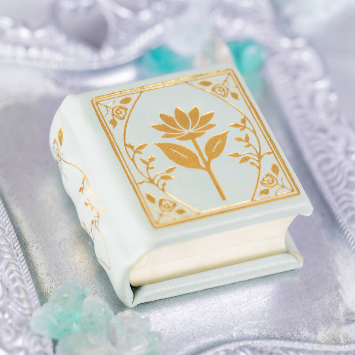 Spring Court Handmade Leather Book Ring Box- Bloomlight Green Edition (Small) by Aquamarise, a delicate white leather ring box with gold floral design on an elegant silver tray.