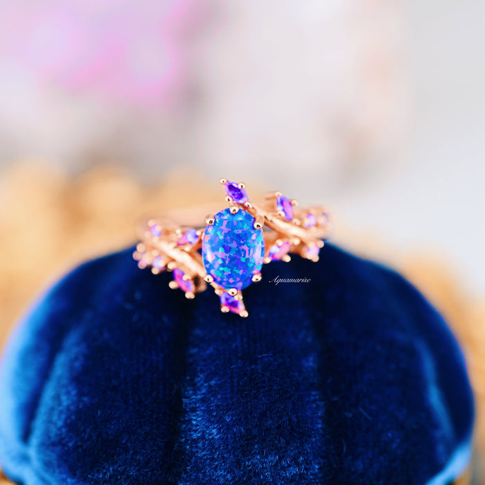 Starry Night Van Gogh Fire Opal & Rose Gold Leaf Couples Ring Set by Aquamarise, featuring a vivid blue and purple fire opal centerpiece with delicate rose gold leaf and violet gemstone accents, displayed on a deep blue velvet cushion.