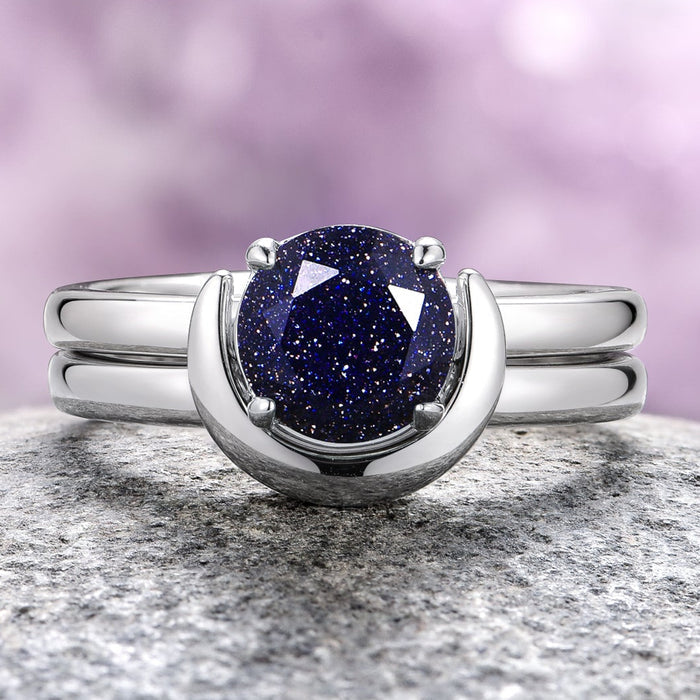 An engagement ring set featuring a crescent moon design with a blue starry center stone, placed on a rock surface.