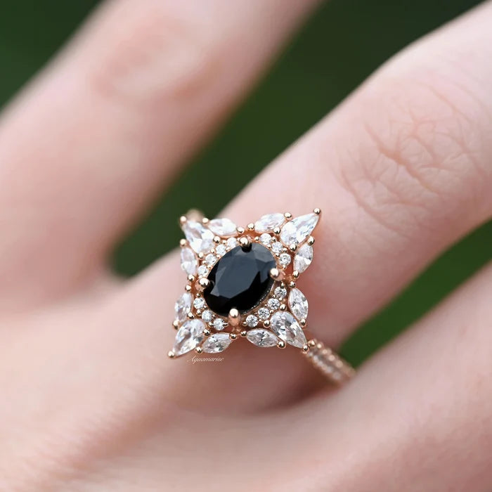 Stella Black Onyx Ring- 14K Rose Gold Vermeil by Aquamarise, featuring an oval black onyx center with a vintage-inspired halo of marquise and pear-shaped stones on a hand.