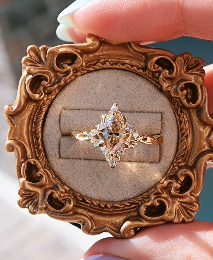 Gold ring with diamonds displayed in an ornate gold frame.