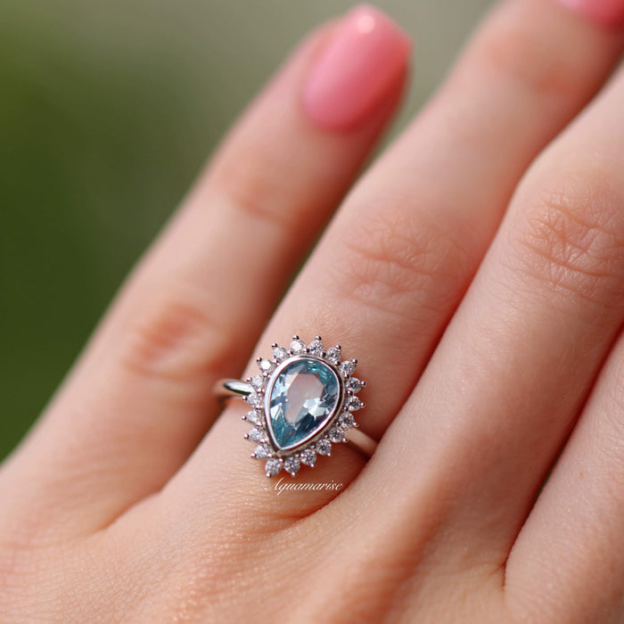 Teardrop Bezel Aquamarine Ring in Sterling Silver featuring a lab-created aquamarine surrounded by sparkling cubic zirconia, showcased on hand by Aquamarise in a vintage-inspired design.