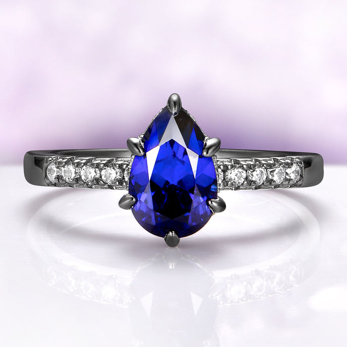 Art Deco Pear Blue Sapphire Ring Set in Black Ruthenium by Aquamarise, featuring a pear-shaped blue sapphire and pavé white stones on a sleek black ruthenium band.