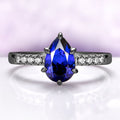 Art Deco Pear Blue Sapphire Ring Set in Black Ruthenium by Aquamarise, featuring a pear-shaped blue sapphire and pavé white stones on a sleek black ruthenium band.