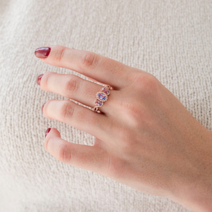 Hand wearing a rose gold ring with a pink gemstone on a light background