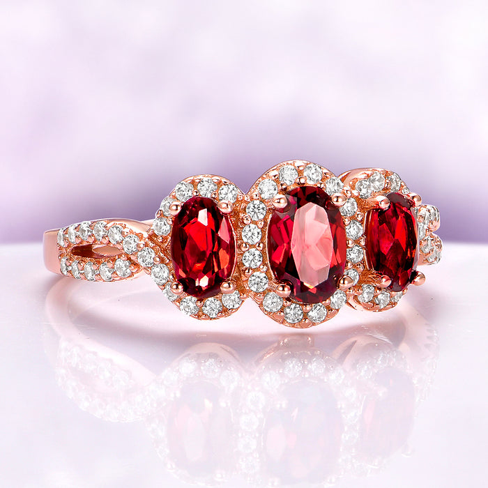 Three Stone Garnet Engagement Ring in 14K Rose Gold Vermeil by Aquamarise featuring three vibrant garnet gemstones surrounded by sparkling white stones on an intricate rose gold band.