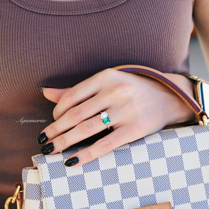 Toi Et Moi Emerald and Moissanite Ring- 14K White Gold featuring an emerald-cut green emerald and pear-shaped moissanite on a white gold band by Aquamarise Gold, styled on a hand holding a patterned bag.