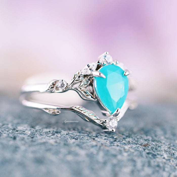 Turquoise Opalescent Blue Sapphire Ring Set in Sterling Silver features a pear-shaped turquoise blue sapphire set in intricate 925 sterling silver with leaf-inspired detailing and small sparkling accent stones by Aquamarise.