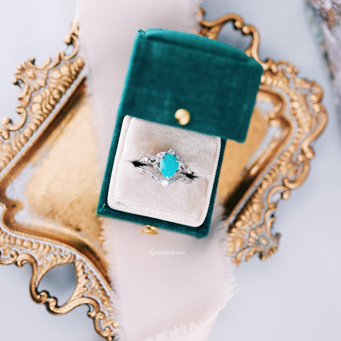 Turquoise Opalescent Blue Sapphire Ring Set in Sterling Silver displayed in a green velvet box, featuring a pear-shaped turquoise blue sapphire surrounded by delicate sterling silver leaf motifs, by Aquamarise.
