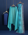 Unstitched turquoise Katan silk suit set with banded geometric stripes on the top and dense paisley-like floral block print on the dupatta, finished with a decorative border strip and fringed ends.