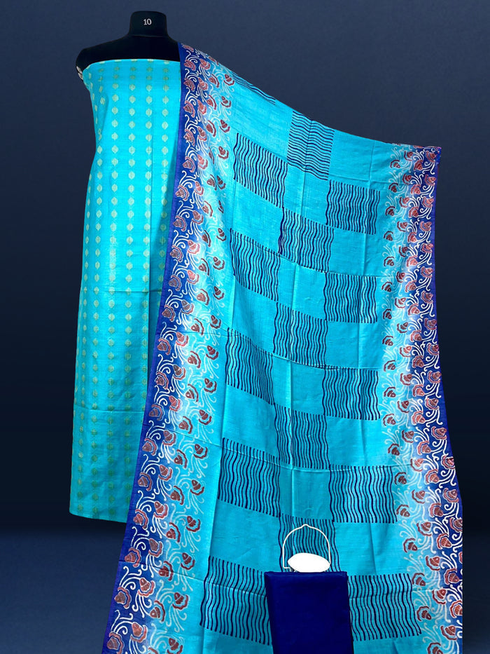 Unstitched turquoise Katan silk suit set with banded geometric stripes on the top and dense paisley-like floral block print on the dupatta, finished with a decorative border strip and fringed ends.