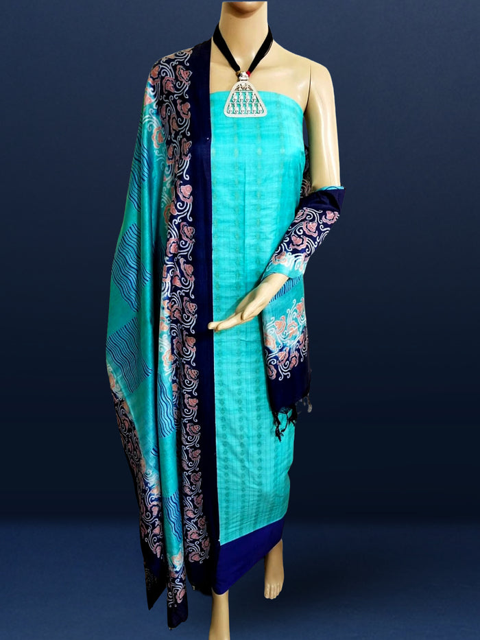Unstitched turquoise Katan silk suit set with banded geometric stripes on the top and dense paisley-like floral block print on the dupatta, finished with a decorative border strip and fringed ends.