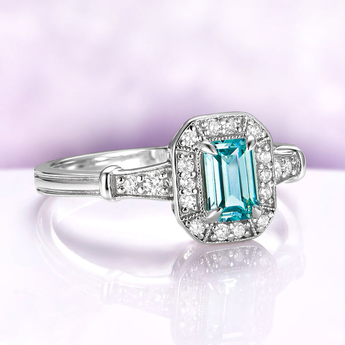 Vintage Halo Aquamarine Ring in Sterling Silver by Aquamarise, featuring a natural emerald-cut blue aquamarine center with a milgrain-edged halo and pavé-set shoulders in a vintage style.