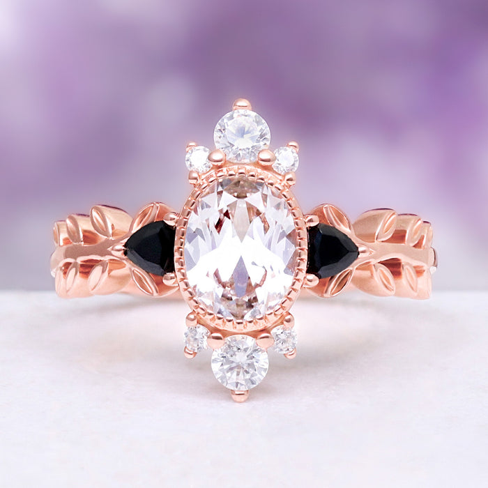Oval lab-grown white sapphire engagement ring with trillion black onyx side stones on a carved leaf band in 14K rose gold vermeil
