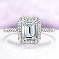 Diamond ring with emerald-cut center stone and halo on a light purple background