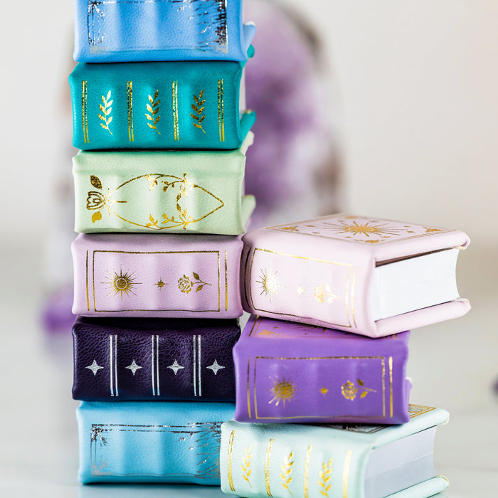 Stack of colorful handmade leather book ring boxes with gold embossed detailing, featuring Spring Court Handmade Leather Book Ring Box- Bloomlight Green Edition (Small) by Aquamarise.