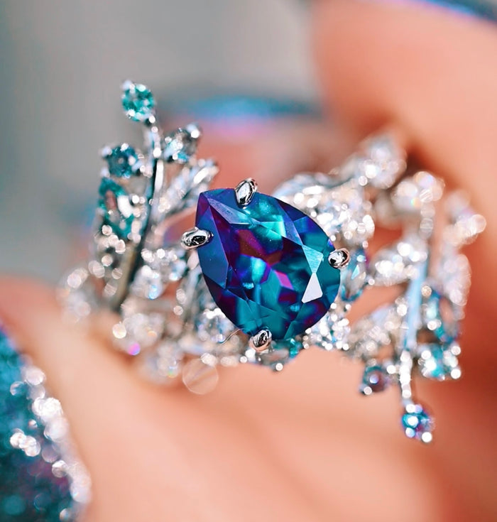 Wisteria Alexandrite Fairy Leaf Ring- 14K White Gold (Two Piece) by Aquamarise Gold features an oval alexandrite center stone with shimmering shades of blue and purple, set in a delicate white gold band with intricate leaf and floral motifs, part of Solid Gold Engagement Rings, June Birthstone Jewelry, and Nature-Inspired Engagement Rings collections.