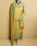 Solid yellow katan silk unstitched suit set with a teal block-printed floral and leaf border running the length of a fringed dupatta.